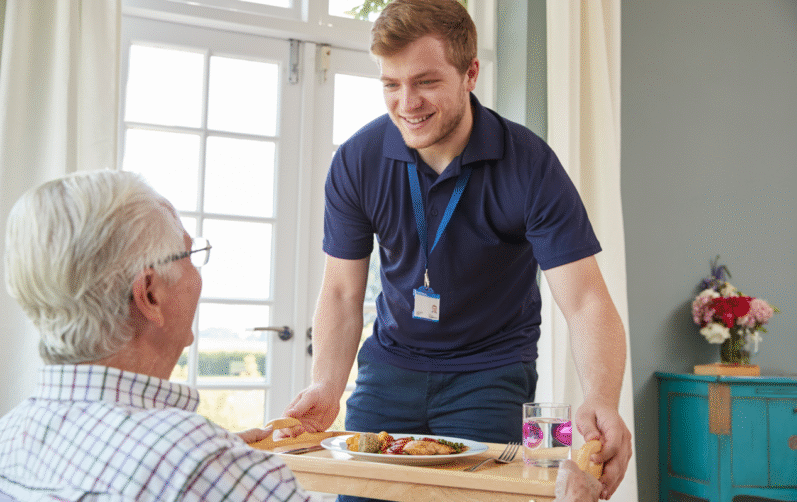 Person som lämnar över en matbricka till en äldre person.